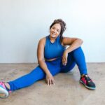 Smiling woman in blue sportswear sitting on the floor demonstrating physical fitness for every body